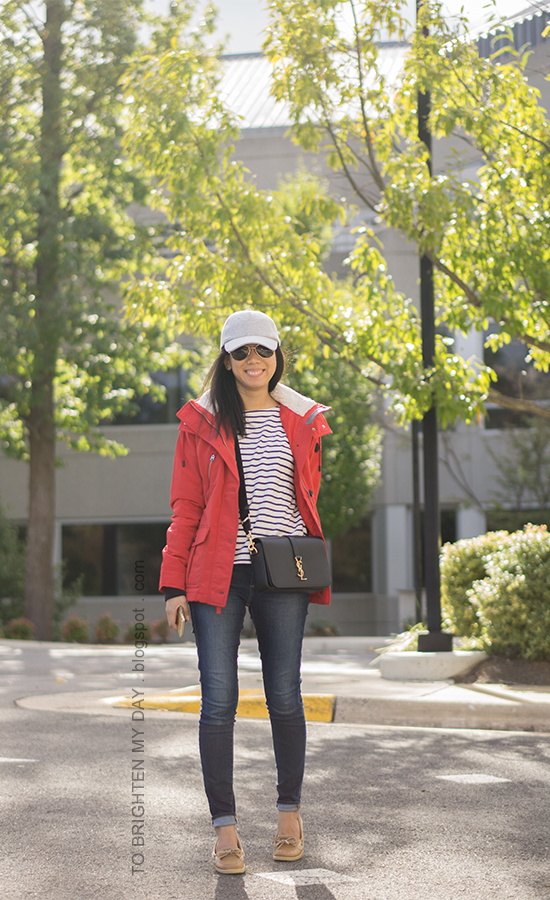gray baseball cap, red performance jacket, striped top, black crossbody bag, skinny jeans, boat shoes